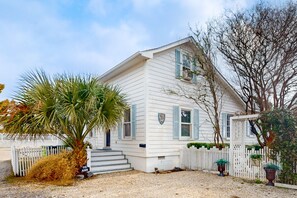 A white house with blue shutters, a front porch, and a small garden with a palm tree. - Historic dog-friendly home with Central AC, Gas Grill and Cozy Patio (Beaufort)