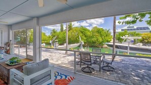A spacious room with large windows, a ceiling fan, a dining area with a table and chairs, and a view of boats and greenery outside. - 3-bedroom waterfront house in fabulous Cudjoe Key (Cudjoe Key)