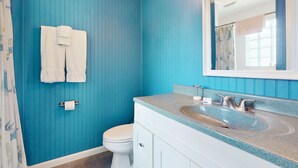Un baño con paredes azules, un inodoro blanco, un lavamanos con espejo y dos toallas blancas colgadas en la pared.