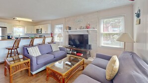 Una sala de estar moderna con sofá, mesa de centro y televisor, junto a una cocina con microondas y chimenea.