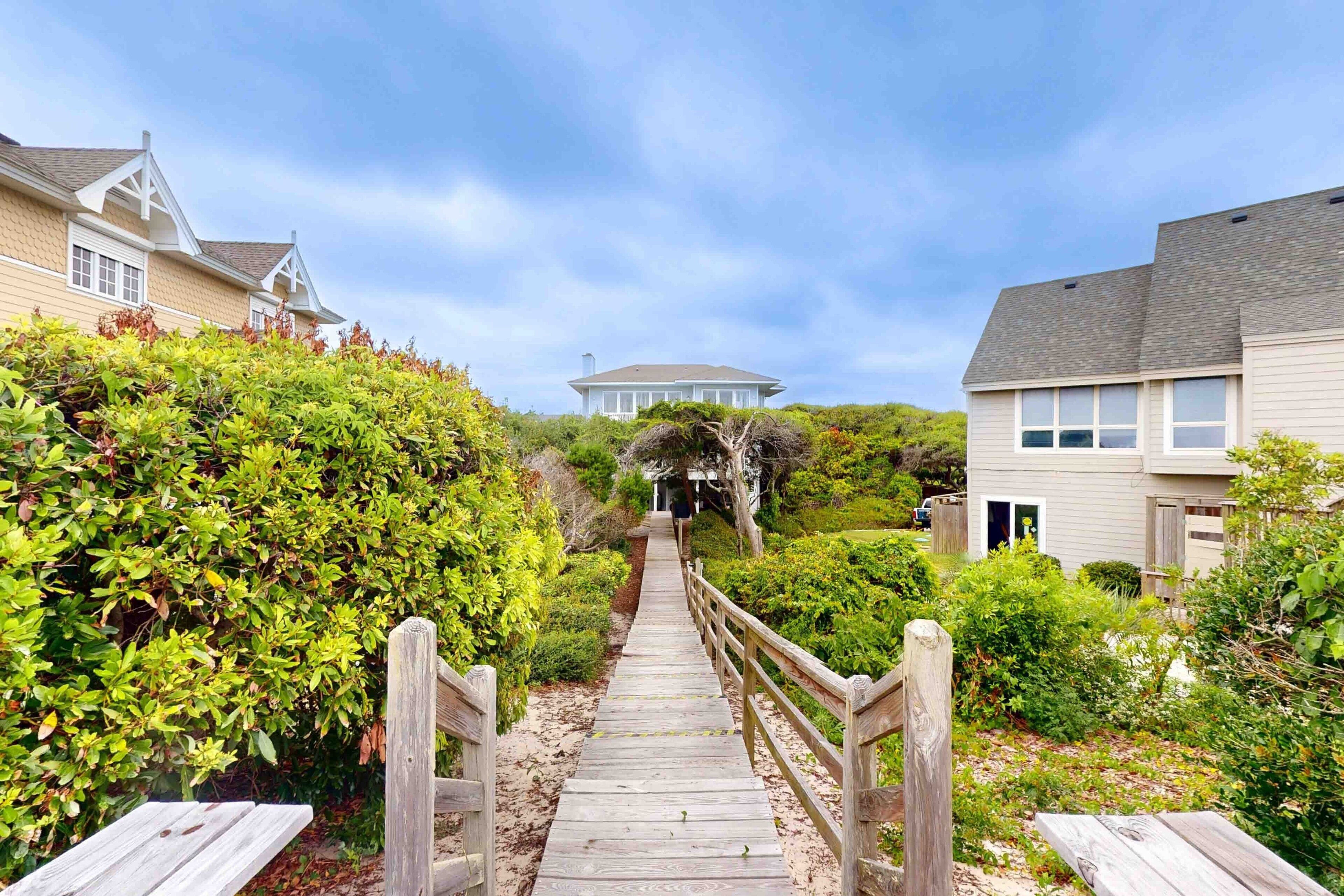 A wooden pathway leading to a house with a gabled roof and a covered porch.