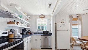 A modern kitchen with white cabinetry, a black countertop, a stainless steel dishwasher, and a dining area with a wooden table and wicker chairs. - Mermaid Cove:  Minutes to beach (Atlantic Beach)