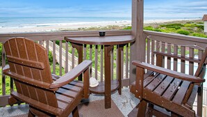 A wooden deck with two Adirondack chairs and a small table, overlooking a beach with a clear view of the ocean and distant shoreline. - Beautifully Remodeled, Oceanfront, 3rd-Floor Condo with Balcony & Shared Pools (Atlantic Beach)
