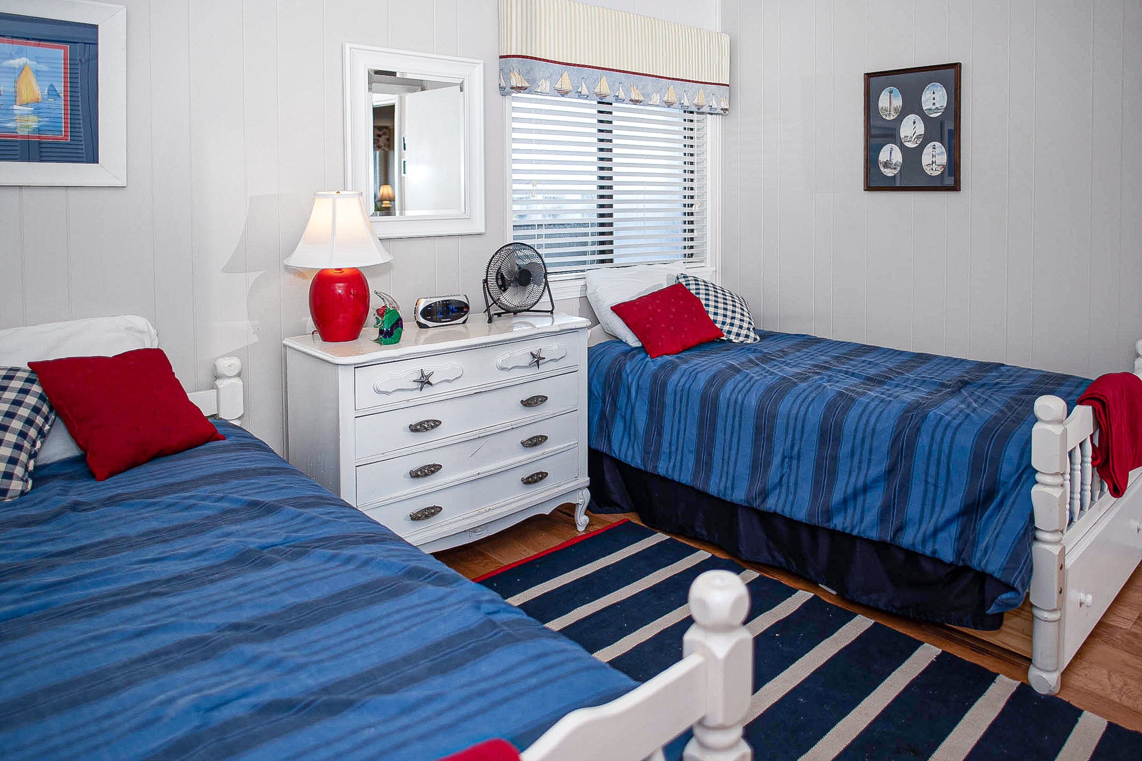 A bedroom with two beds, a dresser, a mirror, and a window with blinds.