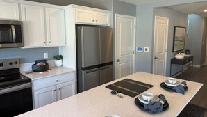 A modern kitchen with white cabinetry, stainless steel appliances, and a central island with a coffee setup. - Bright 4-bedroom house with AC in Lathrop (Lathrop)