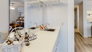 A modern kitchen with white cabinetry, a large island with a sink, and a dining area visible in the background. - Oceanfront, 2nd-Floor Condo with Balcony, WiFi & Shared Hot Tub/Pools/Putt-Putt (Atlantic Beach)