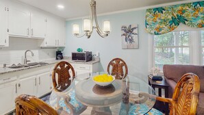 A modern kitchen with white cabinets, a glass dining table with a bowl of lemons, and a wooden chair.