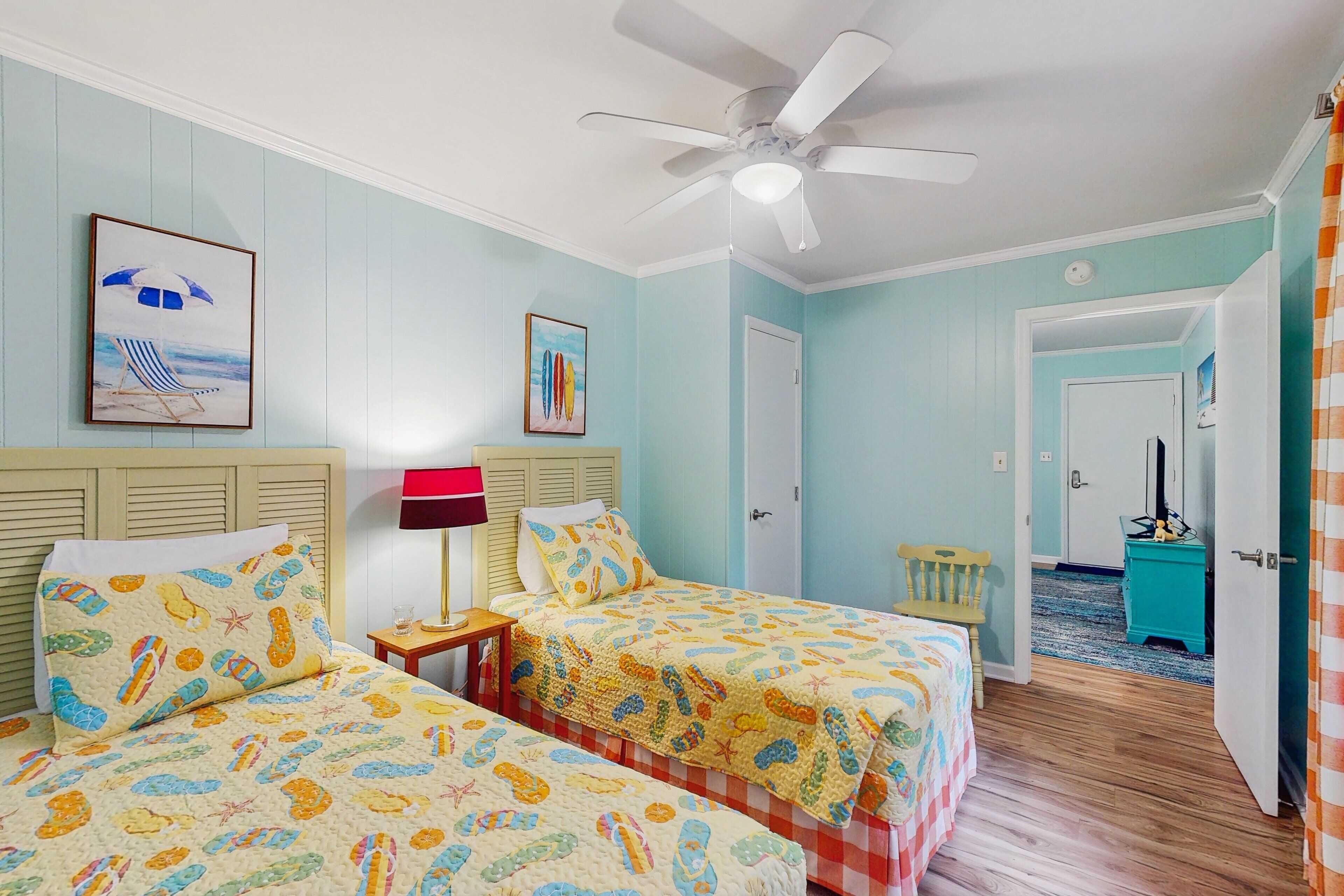 A room with two beds, a ceiling fan, and a door leading to another room.