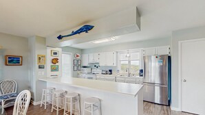 A modern kitchen with white cabinetry, a stainless steel refrigerator, and a bar area with stools.