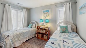 A bedroom with two beds, each with a striped bedspread and matching pillows, a nightstand with lamps, and a framed picture on the wall.