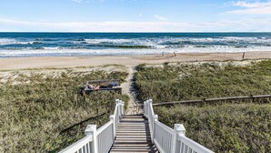 A wooden staircase leading to a beach with a sandy path and a fence.