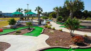 A miniature golf course with green artificial turf, white pathways, and palm trees. - First-Floor Condo with Balcony, WiFi & Shared Pools, Hot Tub, Tennis, Putt-Putt (Atlantic Beach)