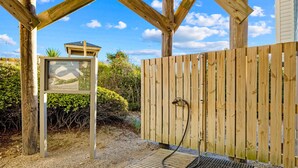 A wooden deck with a shower area, a signboard, and a wooden fence. - Oceanfront condo with shared pool, beach access and ocean views (Atlantic Beach)
