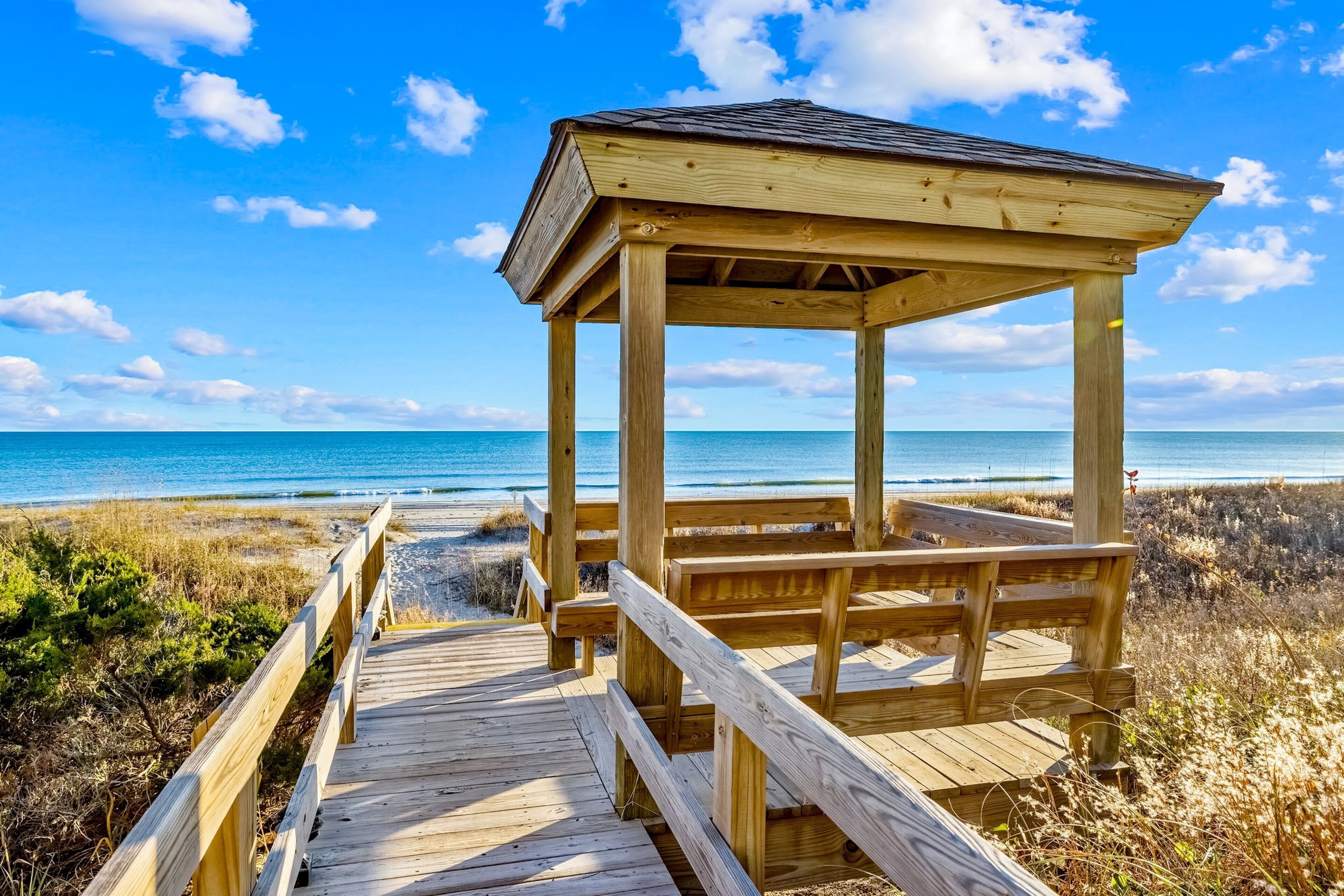 Een houten strandpaviljoen met een houten terras, met uitzicht op een strand en de oceaan.