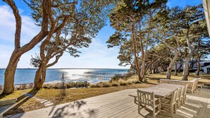 A wooden deck with a table and chairs, overlooking a body of water with a dock in the distance.