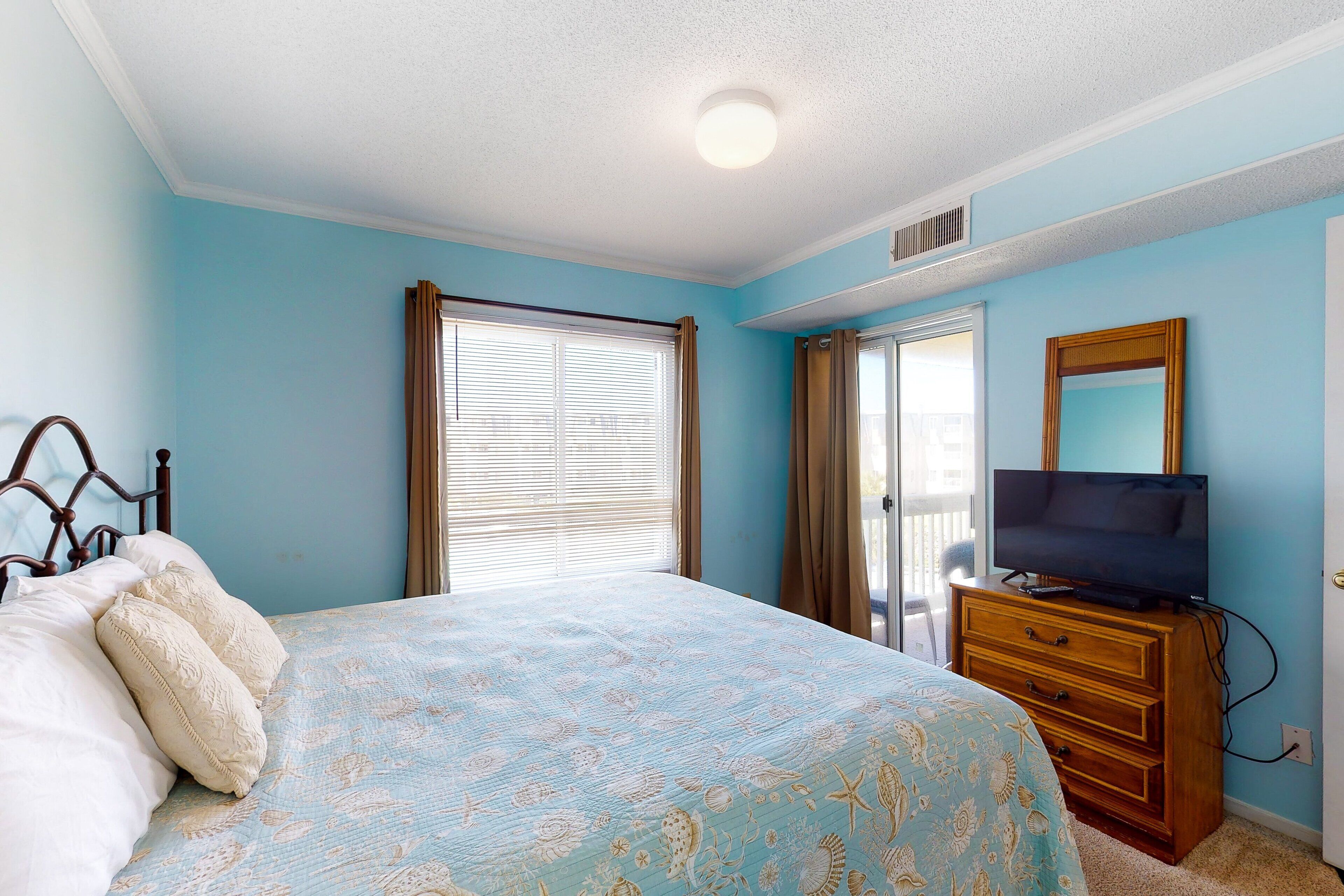 Une chambre à coucher avec un lit, une commode, un téléviseur et une fenêtre avec des rideaux.