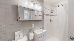 Une salle de bain avec un lavabo blanc, un miroir et un espace douche.