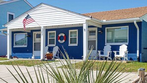 Une maison bleue avec un porche blanc, un drapeau américain et un bouée de sauvetage.