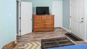 Une pièce avec une commode en bois, un téléviseur posé dessus et un tapis à motifs.