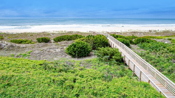 A wooden boardwalk leading to a beach with a clear view of the ocean.