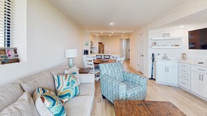 A modern living room with a sofa, patterned armchair, and wooden coffee table. A dining area with a table and chairs is visible in the background. - Stunning Ocean Front Condo with Shared Amenities | Pool, Tennis, and Gym (Atlantic Beach)