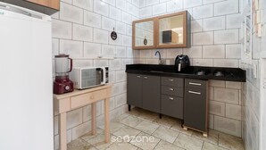 Une cuisine compacte avec des murs recouverts de carreaux blancs, un meuble en bois, un four à micro-ondes, un mixeur et un évier.