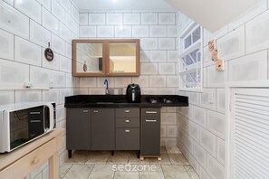 Una cucina compatta con pareti piastrellate di bianco, un piano di lavoro nero, un forno integrato e un armadietto in legno con uno specchio sopra.
