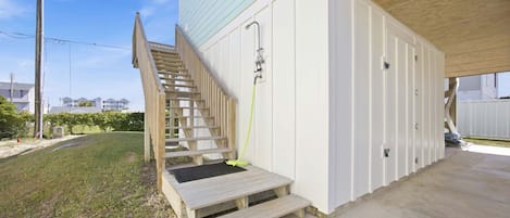 A wooden staircase leading to a covered outdoor area with a hose, a white building with a door, and a concrete floor.