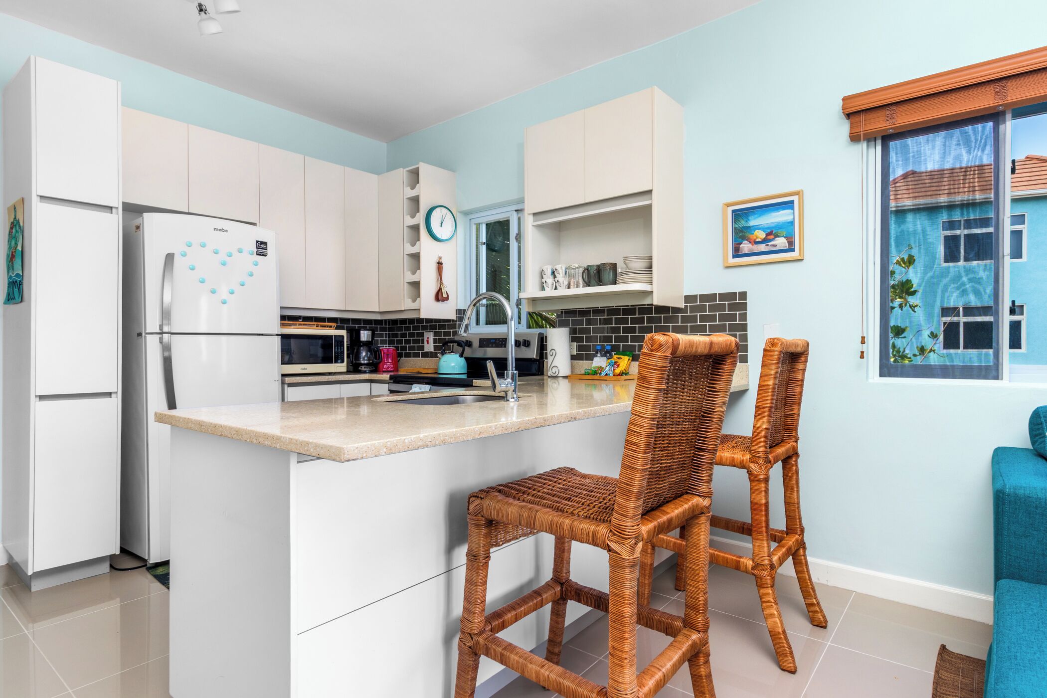Una cocina moderna con armarios blancos, una isla integrada y taburetes de mimbre.