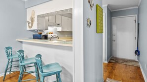 A modern kitchen with white cabinets, a large mirror, and teal bar stools. - 2nd-floor condo with beach access, in/outdoor pools, hot tub, sports courts, AC (Atlantic Beach)