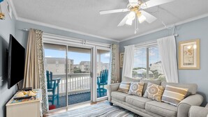 A living room with a sofa, a flat-screen TV, a ceiling fan, and a view through large sliding glass doors to the outside. - 2nd-floor condo with beach access, in/outdoor pools, hot tub, sports courts, AC (Atlantic Beach)