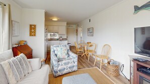 A living room with a sofa, a patterned armchair, a dining table with chairs, and a television. - Remodeled condo with pool, WiFi, W/D & AC - next to state park (Atlantic Beach)