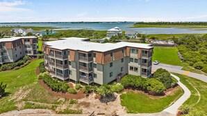 A multi-story residential building with balconies, surrounded by green lawns and a view of a large body of water. - Remodeled condo with pool, WiFi, W/D & AC - next to state park (Atlantic Beach)