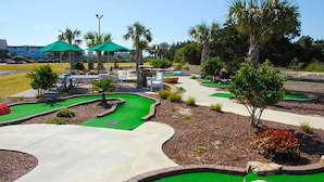 Un parcours de mini-golf avec un gazon artificiel vert, des allées blanches et des palmiers.