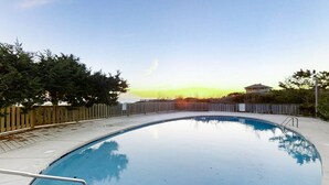 A swimming pool with a wooden fence and trees around it. - Oceanfront, 2nd-Floor Condo with Great Ocean View, Balcony, WiFi & Shared Pool (Pine Knoll Shores)