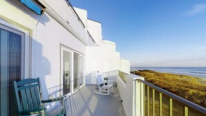 A balcony with a view of the ocean, a green chair, and a white rocking chair. - Oceanfront, 2nd-Floor Condo with Great Ocean View, Balcony, WiFi & Shared Pool (Pine Knoll Shores)