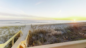A beach with a wooden staircase leading down to the sand, a clear sky, and the sun setting in the distance. - Oceanfront, 2nd-Floor Condo with Great Ocean View, Balcony, WiFi & Shared Pool (Pine Knoll Shores)
