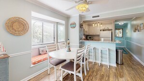 A dining area with a round table, white chairs, and a ceiling fan. - Condo by the ocean with a pool, tennis, WiFi, central AC - steps from the beach (Atlantic Beach)