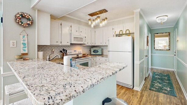 A kitchen with white cabinets, a granite countertop, and a microwave. - Condo by the ocean with a pool, tennis, WiFi, central AC - steps from the beach (Atlantic Beach)