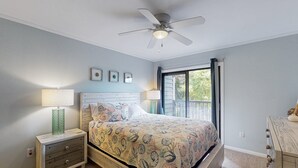 A bedroom with a bed, nightstand, dresser, ceiling fan, and window with curtains. - Condo by the ocean with a pool, tennis, WiFi, central AC - steps from the beach (Atlantic Beach)