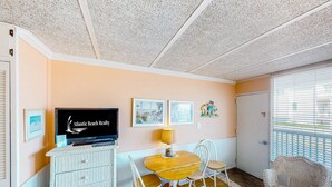 A cozy room with a wooden dining table, white chairs, a television, and framed pictures on the wall. - Shorely Suite #204: Waterfront suite, pool, beach access (Atlantic Beach)