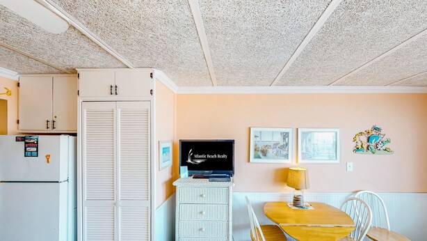 A compact kitchen with a refrigerator, a white cabinet, and a dining table with chairs. - Shorely Suite #204: Waterfront suite, pool, beach access (Atlantic Beach)