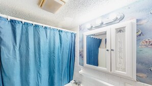 A bathroom with a blue shower curtain, a white sink, and a wall-mounted mirror with a decorative frame. - Shorely Suite #204: Waterfront suite, pool, beach access (Atlantic Beach)