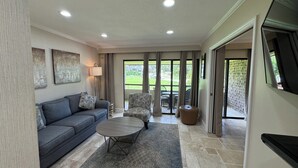 A spacious living room with a grey sofa, a round coffee table, and a patterned armchair. - Pristine 1-bedroom condo w/1.5 Bath in World Renowned Innisbrook Golf Community (Palm Harbor)