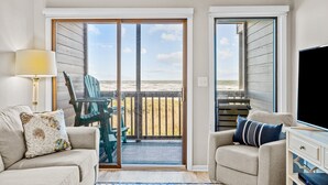 Ein Wohnzimmer mit Blick auf den Strand, inklusive Sofa, Sessel, Fernseher und Lampe.
