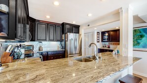 A modern kitchen with dark wooden cabinets, stainless steel appliances, and a granite countertop. - Beautiful 3rd-Floor Oceanfront Condow/Private Balcony & Shared Outdoor Pool (Pine Knoll Shores)
