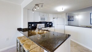A modern kitchen with white cabinets, a granite countertop, a built-in microwave, and a stainless steel refrigerator. - Wonderful condo with private washer/dryer, balcony, and pool/tennis (Atlantic Beach)