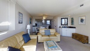 A living room with a sofa, armchair, and coffee table. There is a kitchen in the background with white cabinets and a dining area. - Wonderful condo with private washer/dryer, balcony, and pool/tennis (Atlantic Beach)