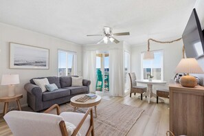 Un salon avec un canapé, des fauteuils, un téléviseur, un ventilateur de plafond et une vue sur l’extérieur, visible à travers une porte.