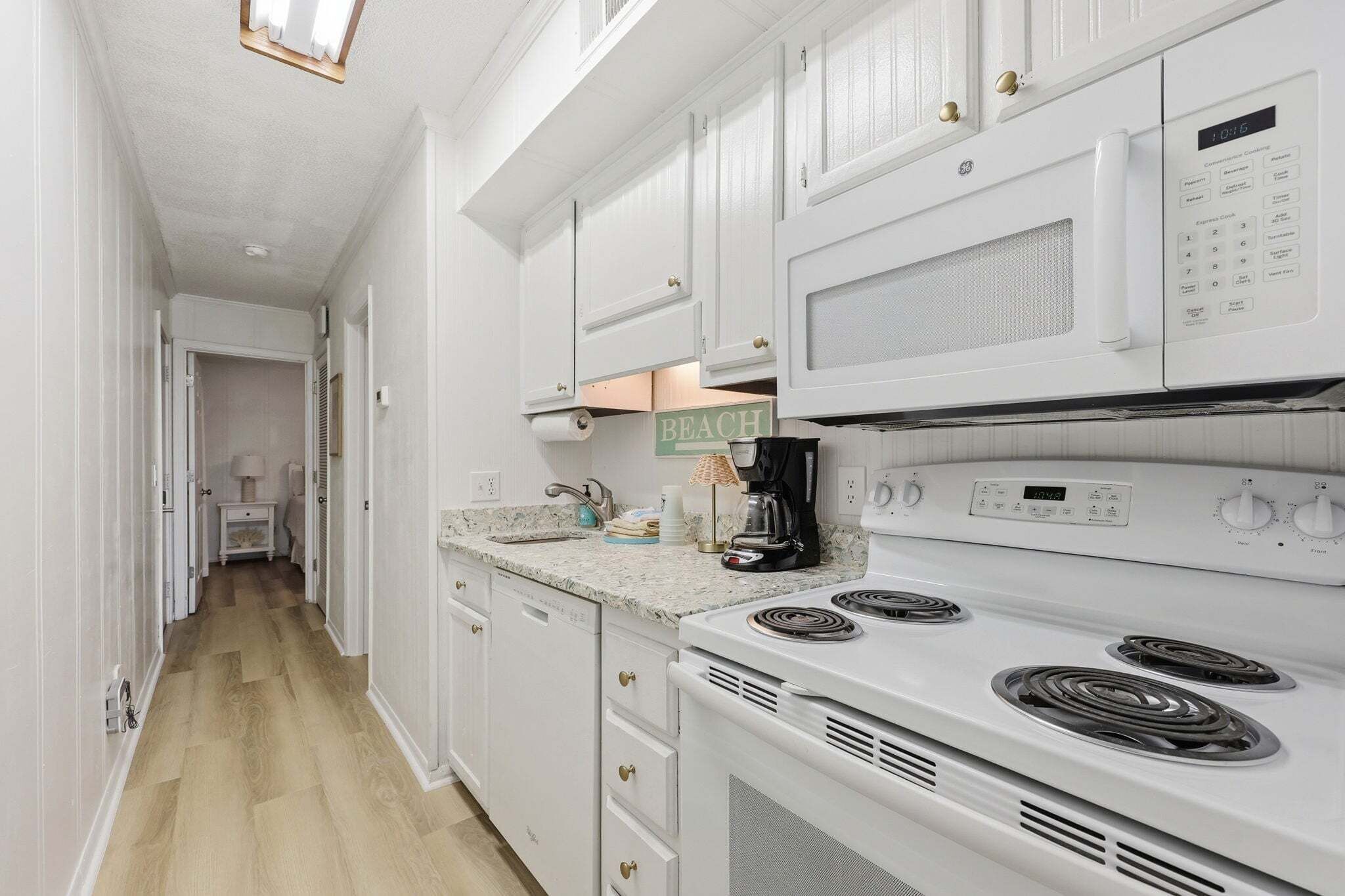 A kitchen with white cabinets, a microwave, a stove, and a coffee maker.